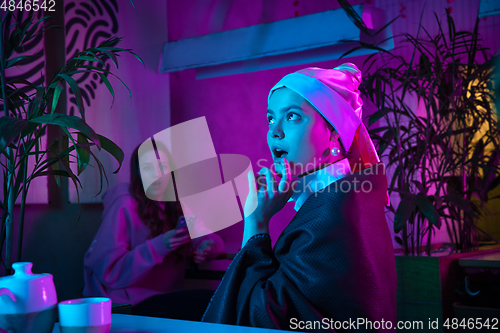 Image of Beautiful girl with a pearl earring taking lunch in modern cafe, restaurant in neon light