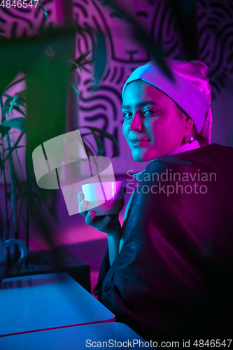 Image of Beautiful girl with a pearl earring taking lunch in modern cafe, restaurant in neon light