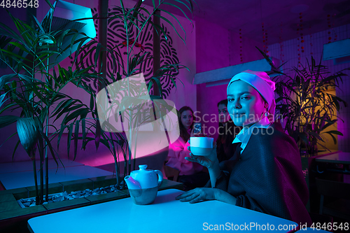 Image of Beautiful girl with a pearl earring taking lunch in modern cafe, restaurant in neon light