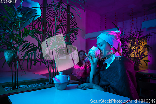 Image of Beautiful girl with a pearl earring taking lunch in modern cafe, restaurant in neon light