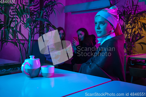 Image of Beautiful girl with a pearl earring taking lunch in modern cafe, restaurant in neon light