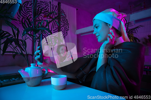 Image of Beautiful girl with a pearl earring taking lunch in modern cafe, restaurant in neon light