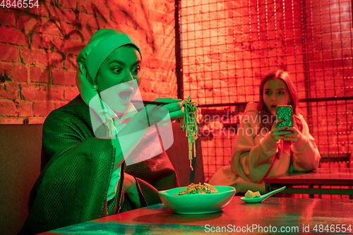 Image of Beautiful girl with a pearl earring taking lunch in modern cafe, restaurant in neon light