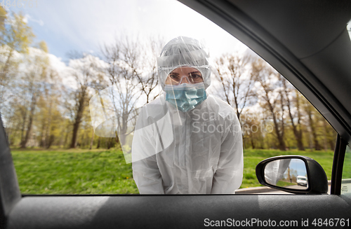 Image of healthcare worker in hazmat suit looking into car