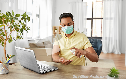 Image of man in mask using hand sanitizer at home office