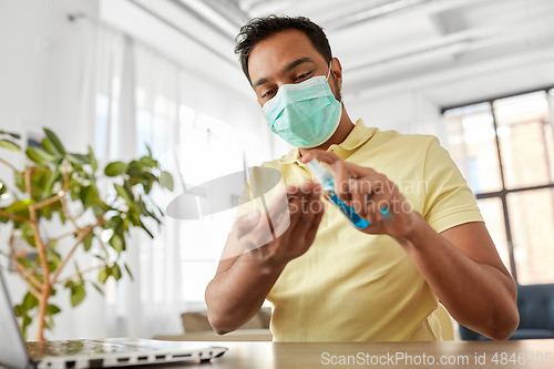 Image of man in mask using hand sanitizer at home office