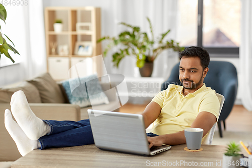 Image of man with laptop resting feet on table at home