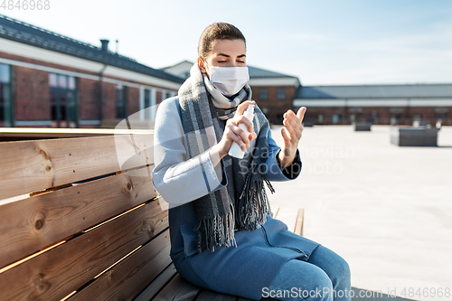 Image of woman in mask spraying hand sanitizer outdoors