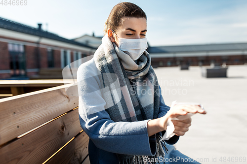 Image of woman in mask cleaning hands with wet wipe in city