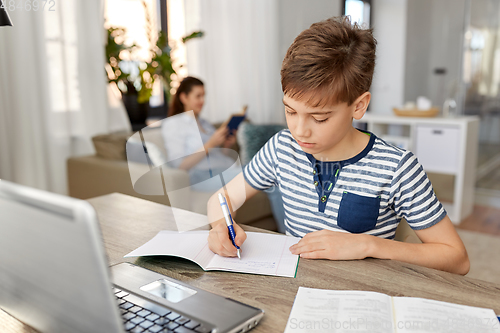 Image of student boy with book writing to notebook at home