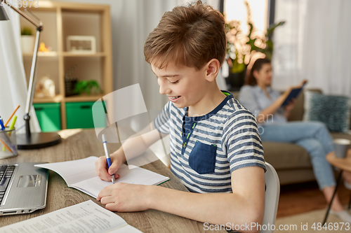 Image of student boy with book writing to notebook at home