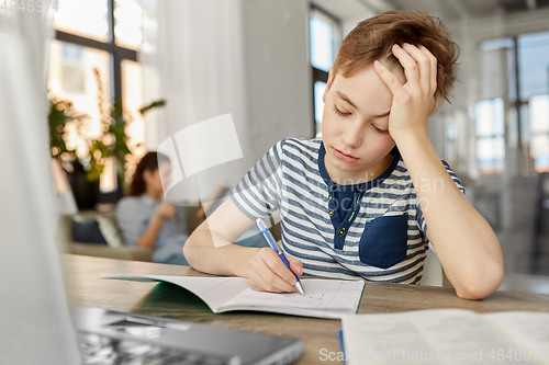 Image of student boy with book writing to notebook at home