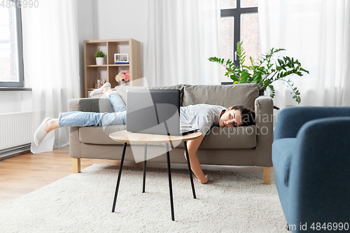 Image of bored woman with laptop lying on sofa at home