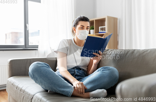 Image of sick woman in medical mask reading book at home