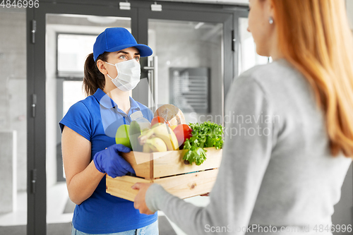 Image of delivery girl in mask giving box of food to woman