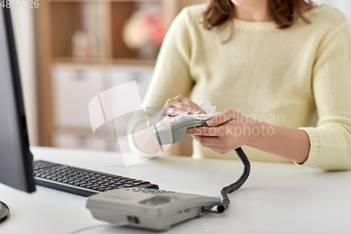 Image of close up of woman cleaning desk phone with tissue