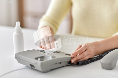 Image of close up of woman cleaning desk phone with tissue