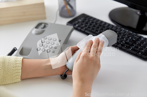 Image of close up of woman cleaning desk phone with tissue