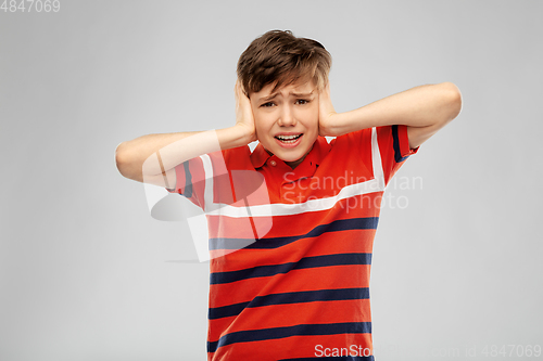 Image of boy closing ears with hands over grey background