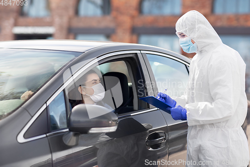 Image of healthcare worker with clipboard and woman in car