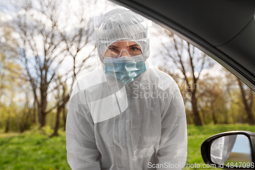 Image of healthcare worker in hazmat suit looking into car