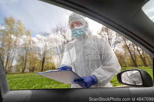 Image of doctor in hazmat suit with clipboard at car