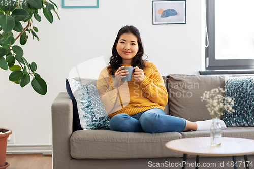 Image of smiling asian young woman drinking coffee at home