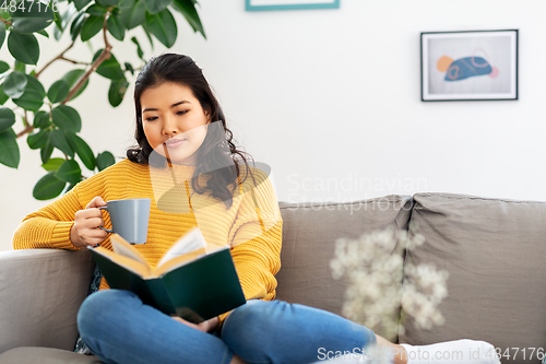 Image of woman reading book and drinking coffee at home