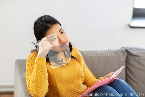 Image of asian woman with diary sitting on sofa at home