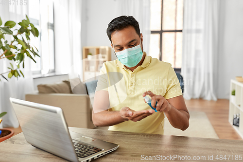 Image of man in mask using hand sanitizer at home office