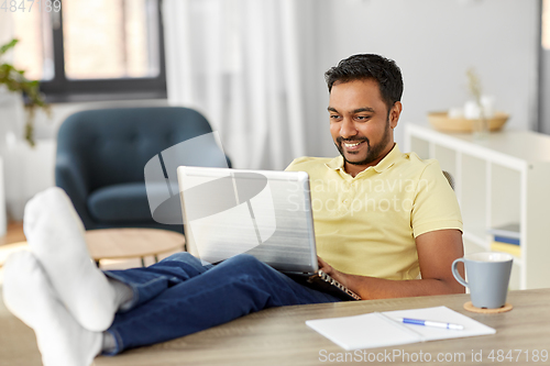 Image of man with laptop resting feet on table at home