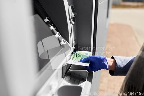 Image of hand in medical glove with money at atm machine