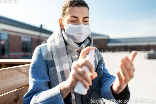 Image of woman in mask spraying hand sanitizer outdoors