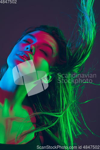 Image of Beautiful woman\'s portrait with blowing hair on dark studio background in colorful neon light