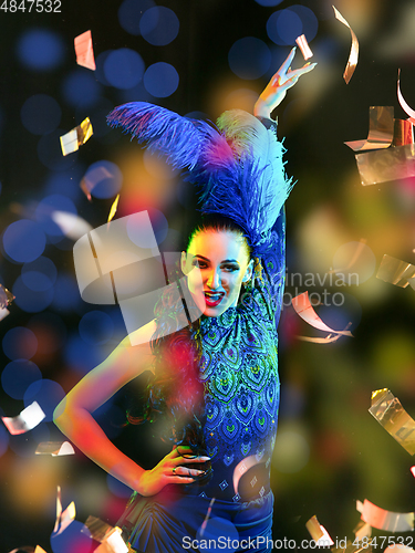 Image of Beautiful young woman in carnival and masquerade costume in colorful neon lights on black background in flying confetti