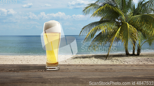 Image of Glass with cold beer with sea or ocean beach on background