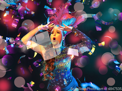 Image of Beautiful young woman in carnival and masquerade costume in colorful neon lights on black background in flying confetti