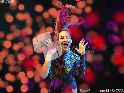 Image of Beautiful young woman in carnival and masquerade costume in colorful neon lights on black background in flying confetti