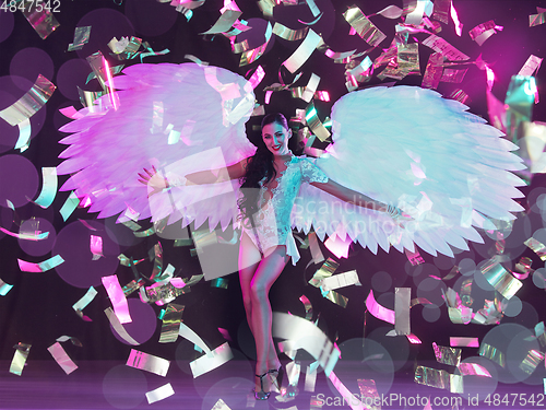 Image of Young female dancer with angel\'s wings in neon light on black background in flying confetti
