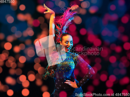 Image of Beautiful young woman in carnival and masquerade costume in colorful neon lights on black background in flying confetti