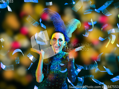 Image of Beautiful young woman in carnival and masquerade costume in colorful neon lights on black background in flying confetti