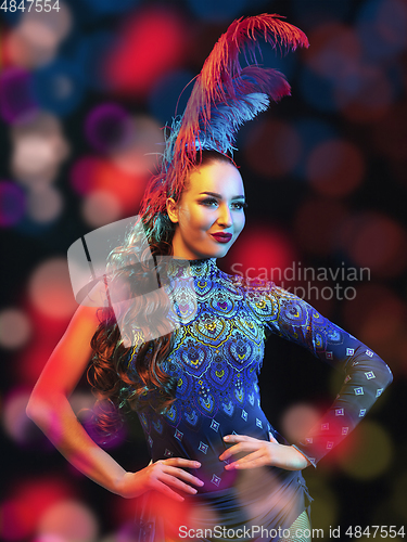 Image of Beautiful young woman in carnival and masquerade costume in colorful neon lights on black background in flying confetti