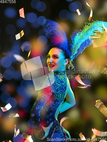 Image of Beautiful young woman in carnival and masquerade costume in colorful neon lights on black background in flying confetti
