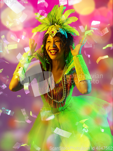 Image of Beautiful young woman in carnival and masquerade costume in colorful neon lights on gradient background in flying confetti