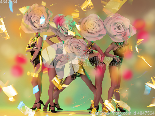 Image of Young female dancers with huge floral hats in neon light on gradient background in flying confetti