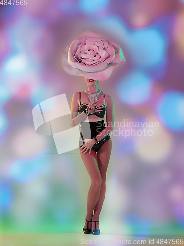 Image of Young female dancer with huge floral hat in neon light on gradient background in flying confetti