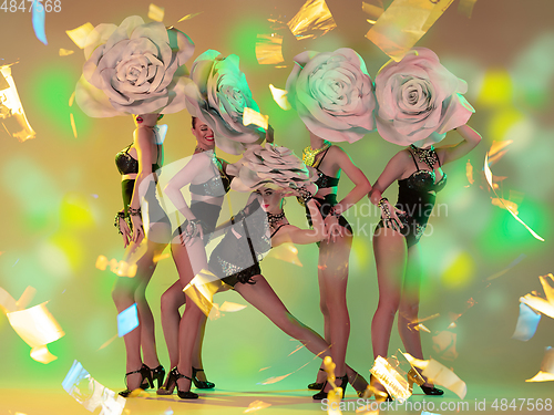 Image of Young female dancers with huge floral hats in neon light on gradient background in flying confetti