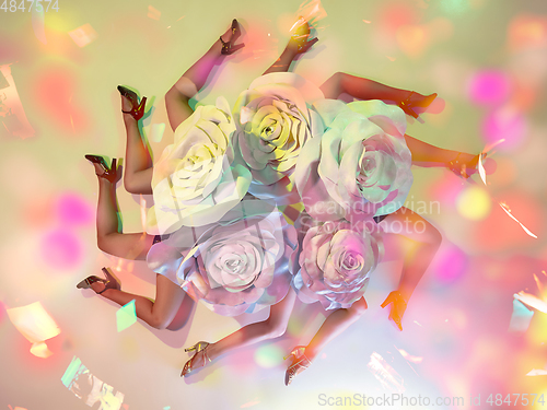 Image of Young female dancers with huge floral hats in neon light on gradient background in flying confetti, top view