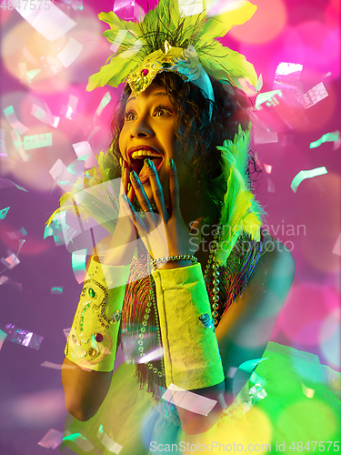 Image of Beautiful young woman in carnival and masquerade costume in colorful neon lights on gradient background in flying confetti