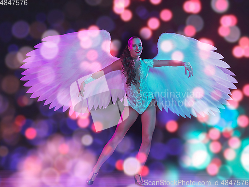 Image of Young female dancer with angel\'s wings in neon light on black background in flying confetti